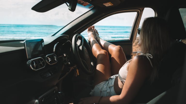 lady sitting in van with feet out the window overlooking ocean